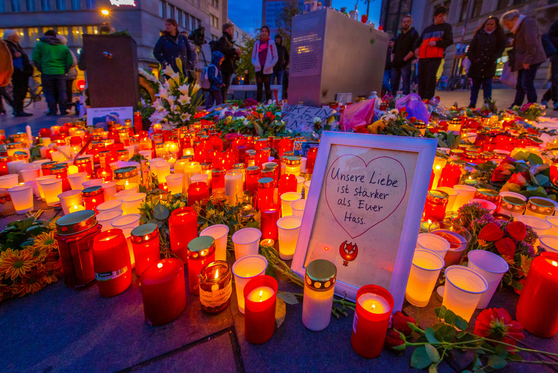 Das Bild zeigt Kerzen auf der Straße in Halle; ferner einen Bilderrahmen mit der Inschrift Unsere Liebe ist stärker als euer Hass.